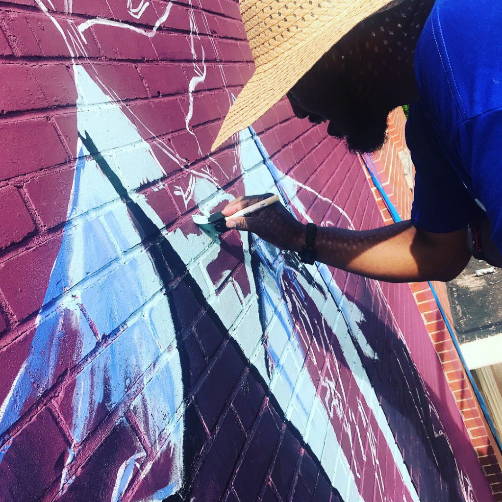 Photojournalist and graphic designer Charles Brice wears a hat to protect him from the torrid sun as he adds his unique touch to the mural of former president Barack H. Obama. The image can be found on the south side wall of Barack H. Obama Magnet School. (Photo special to JSU.)