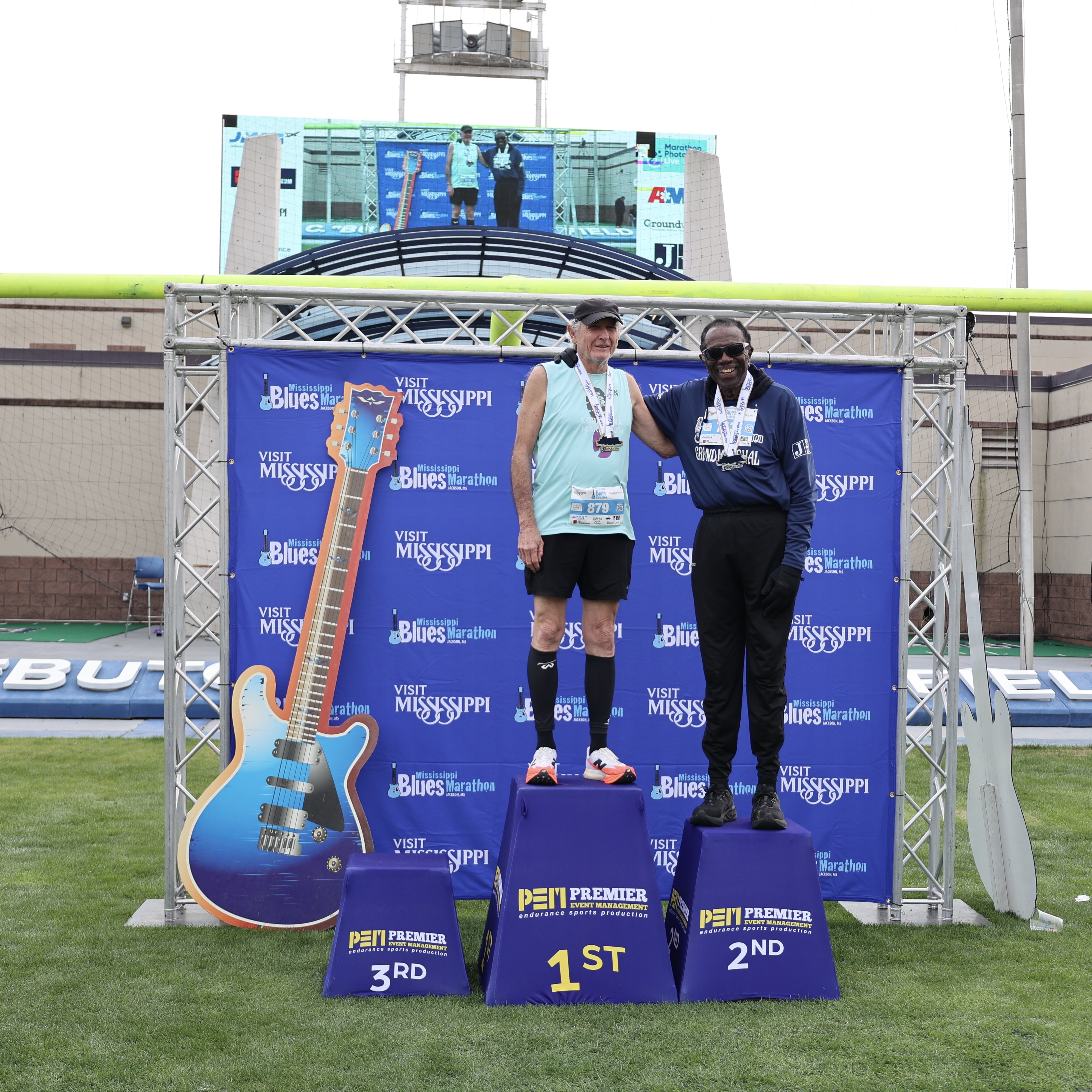 Dr. Hilliard Lackey poses for a photo on the awards podium with the first place winner in his age division in the 1/2 marathon at the 19th Annual Mississippi Blues Marathon